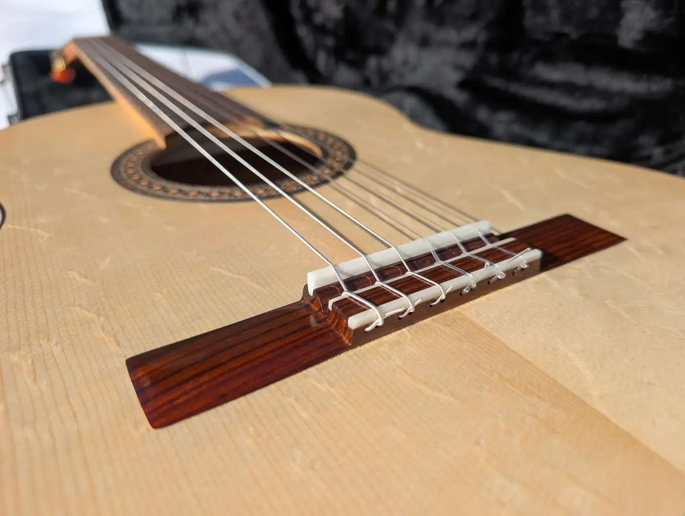 Rosewood bridge with a 12-hole tie block on the alpine spruce soundboard of a Kairòs concert classical guitar, strings running to the bone saddle