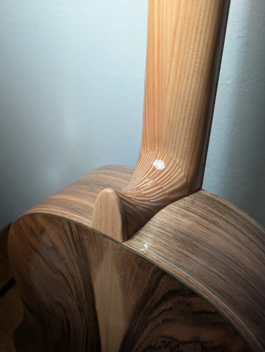 The heel of a Kairòs classical guitar neck meeting the figured walnut back, the French polished surfaces catching the workshop light